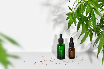 Cosmetic products with CBD oil and hemp extract. Glass bottles with pipette, hemp plant and seeds on table wall background
