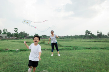 happy little Asian boy with a kite running on meadow in summer in nature