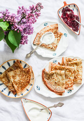 Cozy homemade breakfast on a light background - wholegrain crepes, cranberry jam, lilac bouquet, top view