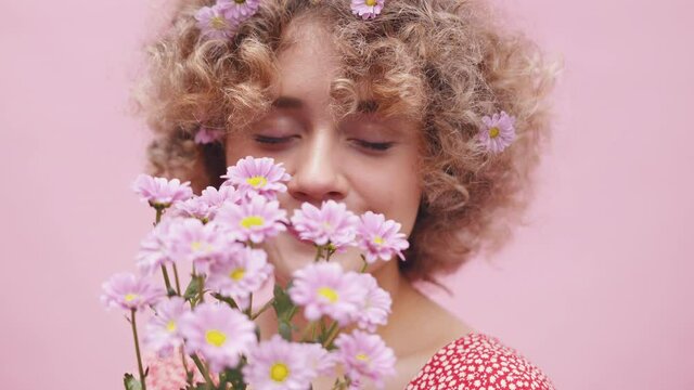 Portrait of a young caucasian woman with bouquet of spring flowers over her face and floral decoration in her curly hair. Close up