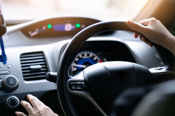 A woman sitting in front of the driver in a black car, using her fingers pressing a function button on the console inside the car, traveling on the road,
