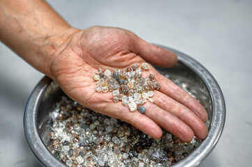 A wide variety of rough diamonds are in the palm of your hand. Many small gems