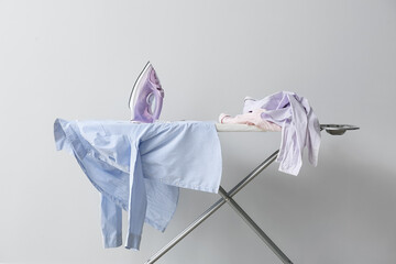 Board with electric iron and  clothes on light background