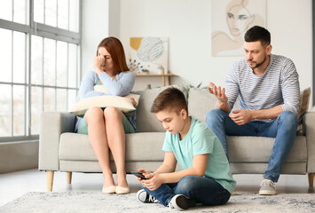 Little boy using mobile phone and his sad parents at home