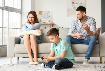 Little boy using mobile phone and his sad parents at home