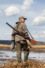 hunter with a duck decoys in both hands stands on the shore