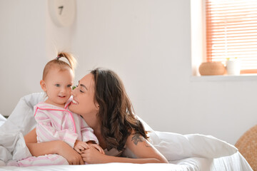 Happy woman and her little daughter sitting on bed at home
