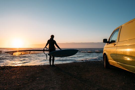Surfer on the background of a colorful sunset and a surfmobile 