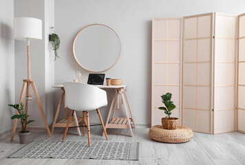 Stylish workplace with laptop and mirror near light wall in room