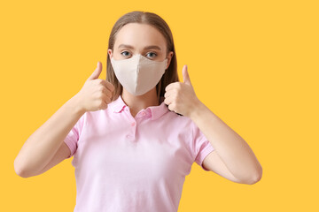 Stylish young woman wearing mask and showing thumb-up on color background