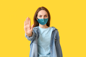 Young woman wearing medical mask and showing STOP gesture on color background