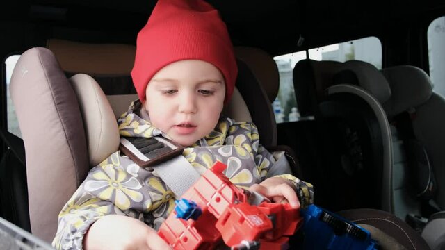 Child in hat and jacket plays with robot sitting in car