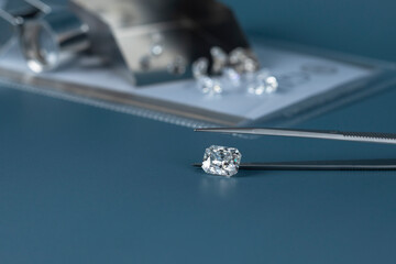 Cut diamond in hand close up with jewelry tools and scattering of different diamonds in background,...