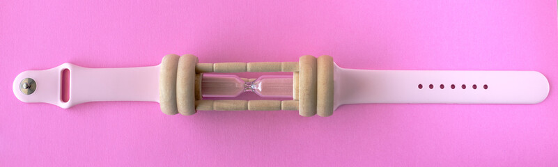 hourglass with a pink silicon wristband from smartwatches on a pink surface 
