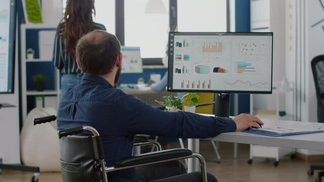 Group of business people discussing company plan typing on computer working for financial project presentation, manager sitting in wheelchair in strat up business office. Man checking company reports