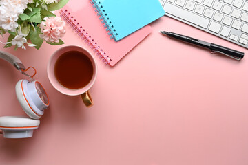 Above view of woman workspace with headphone, coffee cup, notebook, keyboard and flowers on pink pastel background.
