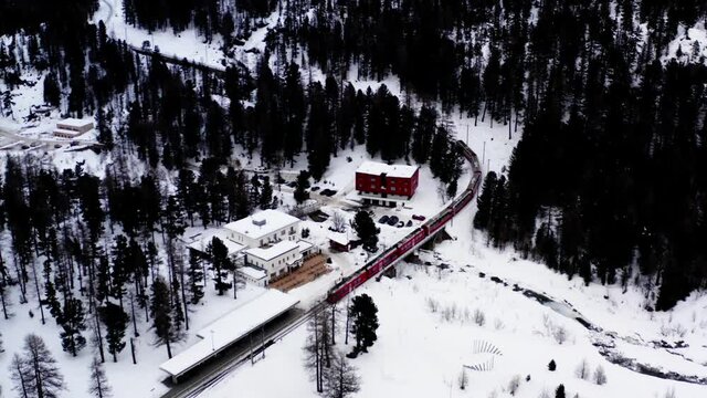 Aerial overlooking from drone camera shooting downhill and read locomotiv transport crossing snowy railway in Scandinavia, bird's eye of track express during travel trip
