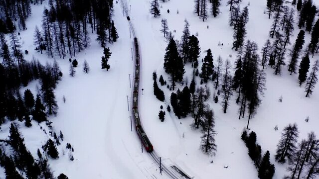 Drone camera shooting red train express crossing snowy environment in foot of high mountains, bird's eye overlooking of railway transportation in Scandinawian Wonderland