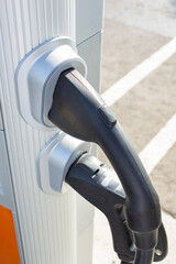 A closeup view of the pump hose of an electric vehicle charger unit, seen in a local parking lot.