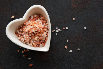 Himalayan pink salt on black background in a heart shape saucer