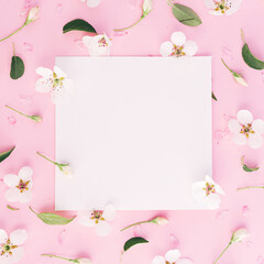 White flowers pattern around white papers with pink paper clip on pink background, copy space in centre, vertical photo, spring time