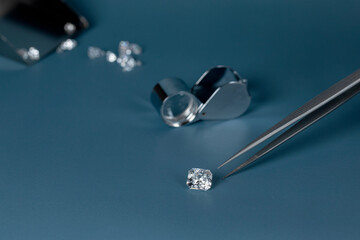 Cut diamond in hand close up with jewelry tools and scattering of different diamonds in background,...