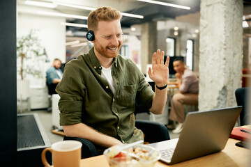 Happy entrepreneur waving during video call over laptop at corporate office.