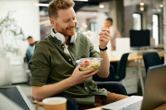 Happy businessman eating salad on lunch break in the office.