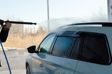 close-up - a white car with black tinted glass at a car wash, a gun spraying high pressure water is visible