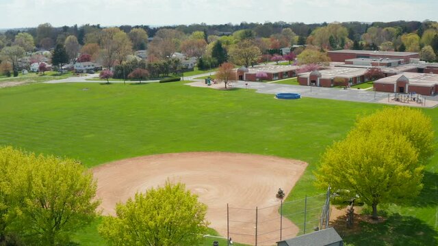 Baseball diamond. Worker prepares field for youth game at school campus. Aerial spring daytime shot.