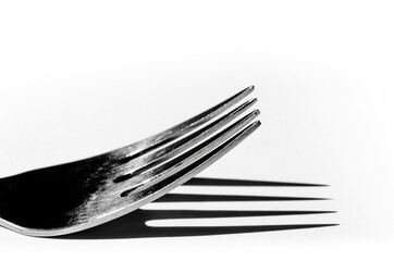 Closeup of a fork horizontally on a white surface, with a harsh shadow