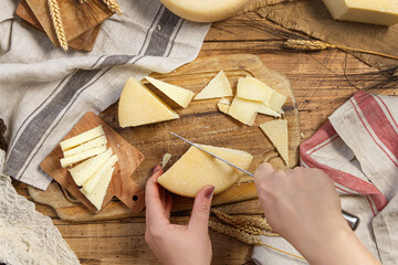 Hands cutting pieces of  fresh homemade cheese on a wooden board