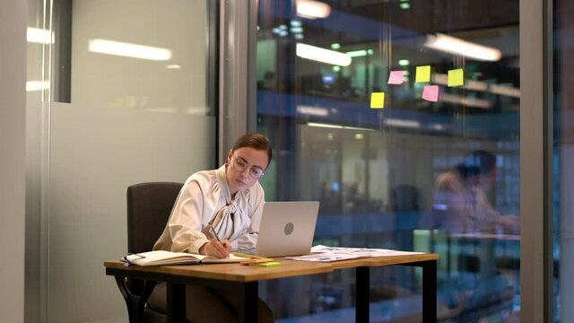 Caucasian employee in optical spectacles writing mail message on modern laptop computer while creating business plan for startup project working in office interior, skilled manager using cellphone