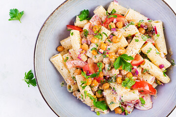 Vegetarian vegetable pasta. Pasta rigatoni with tomato, red onion, parsley and fried chickpeas with nut sauce. Vegan food. Top view, overhead