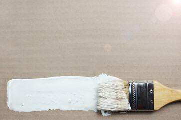 Brush stroke with white paint on brown cardboard. The theme of finishing works, construction, wood...