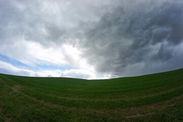 Dark thundercloud approaching the blue sky over the green field