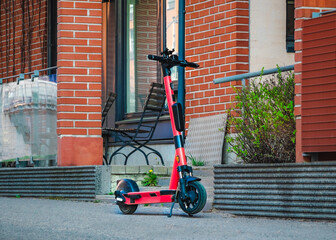 Electric kick scooter for rental parked on sidewalk of street in front of brick wall building. E-scooter for public sharing in European city center. Urban Transportation Concept. Rent eco transport.