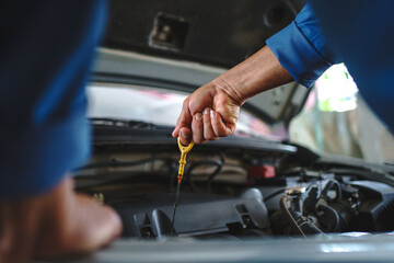 Auto mechanic is checking the engine oil in a vehicle at the garage. Maintenance concept.
