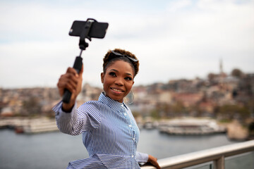  Beautiful african woman taking a selfie in modern city. Cute young woman taking a selfie on a bridge.