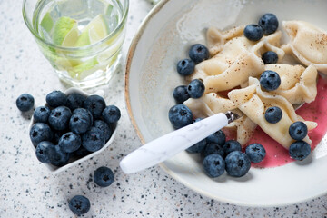 Vareniki or dumplings with cottage cheese and fresh bilberries in a beige plate, closeup, selective focus