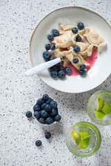 Plate of cottage cheese dumplings with bilberries, above view on a beige stone background, vertical shot with space