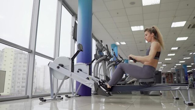 Young woman working out on row machine at gym exercising