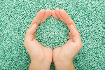 Young adult woman palms holding green complex fertiliser granules for vegetables, flowers and...