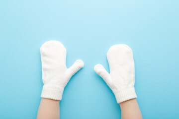 Baby hands in white warm mittens on light blue table background. Pastel color. Closeup. Point of view shot. Top down view.