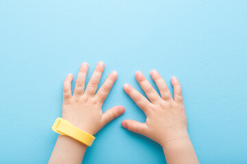 Yellow mosquito repellent band on baby wrist on light blue table background. Pastel color. Closeup. Point of view shot. Protection from insects. Top down view.