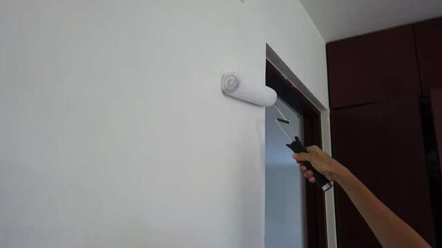 Painting a wall with white roller brush on a room