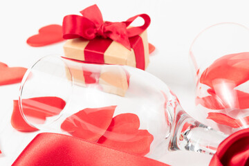 two champagne glasses, a box with a gift, a red silk ribbon and a lot of hearts scattered on a white wooden table. close-up