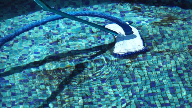 Vacuuming the dirty bottom of a swimming pool. A special brush with a striped hose cleans the pool. Hose of cleaning machine working in pool under water.