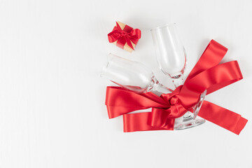two champagne glasses, a gift box and a red silk ribbon on a white wooden table. close-up