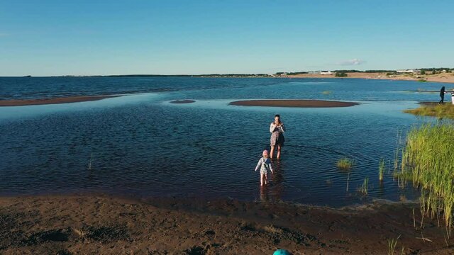Aerial view around a mom taking pictures of kids playing at a beach, in Finland